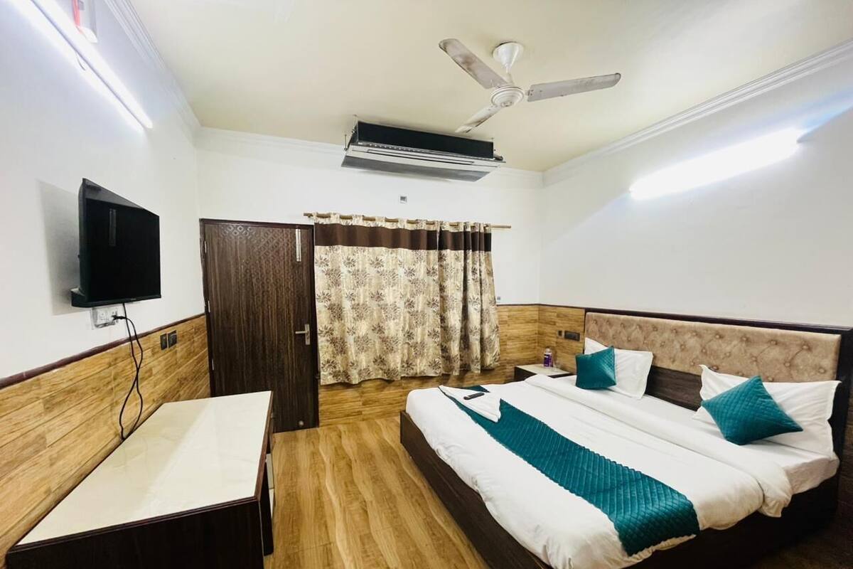 Une chambre d’hôtel équipée d’un lit, d’une table de chevet, d’une télévision, d’un climatiseur et d’un ventilateur de plafond.