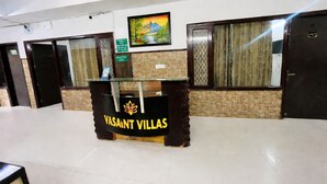 En receptionsdisk med et skilt der siger 'VASANT VILLAS' og et indrammet billede over.
