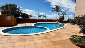 Zona de piscina con dos piscinas, un edificio y cielo despejado.
