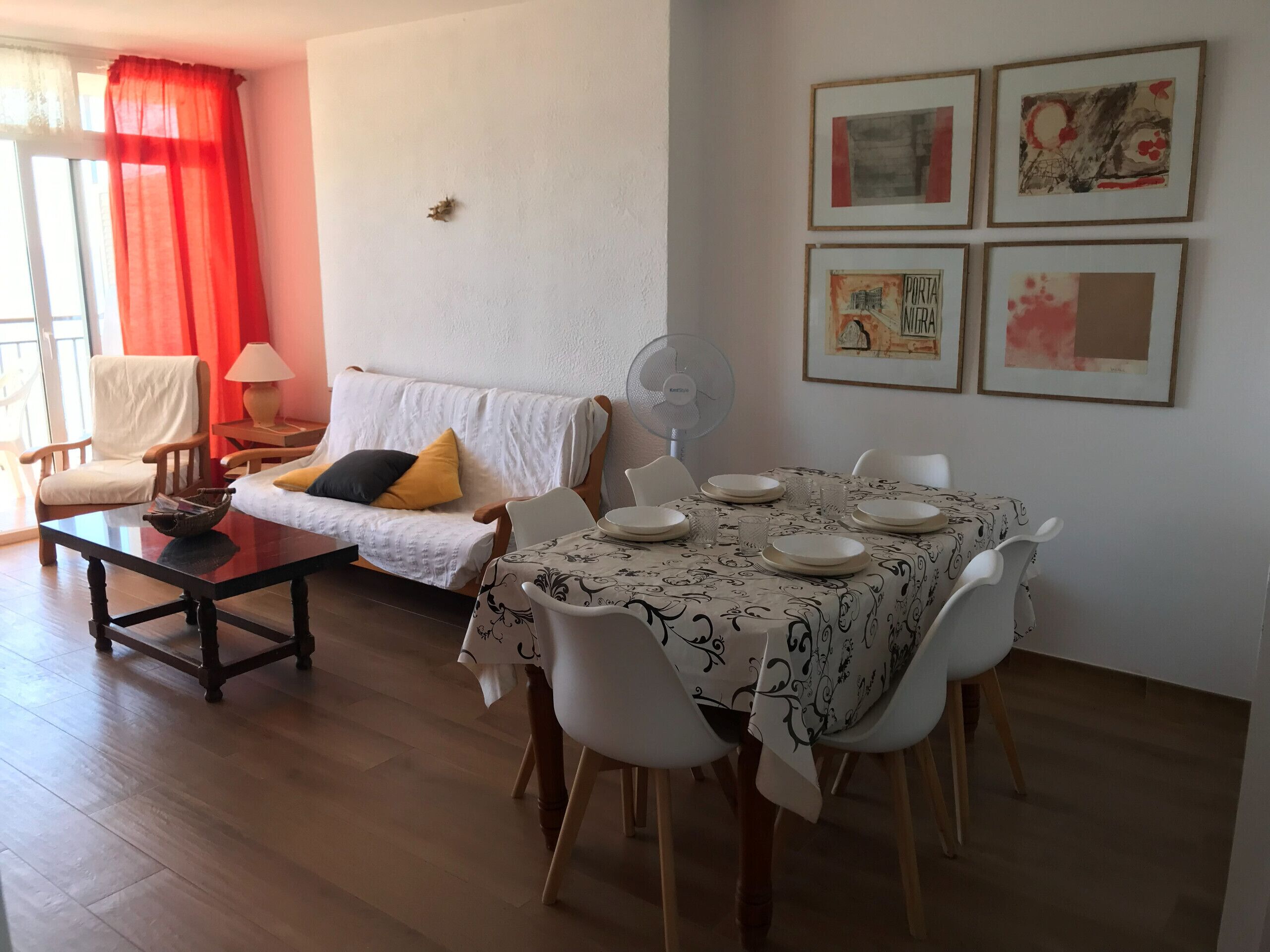 Een woonkamer met een bank, een eettafel voor vier personen en een ventilator.