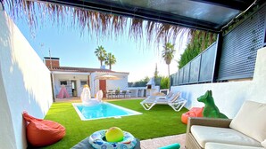 Ein Garten mit Swimmingpool, Kunstrasen, Liegestühlen und einer Rattan-Couch.