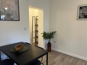 Ein Zimmer mit einem dunklen Holztisch, einer Pflanze, einer Leiter und einem gerahmten Bild an der Wand.