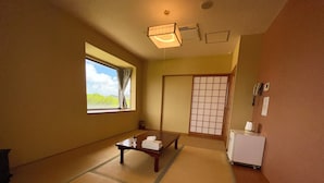 A room with tatami mats, a low table with a towel, a small refrigerator, and a shoji screen. - Enagic OKinawaInternational Youth Hostel (Naha)