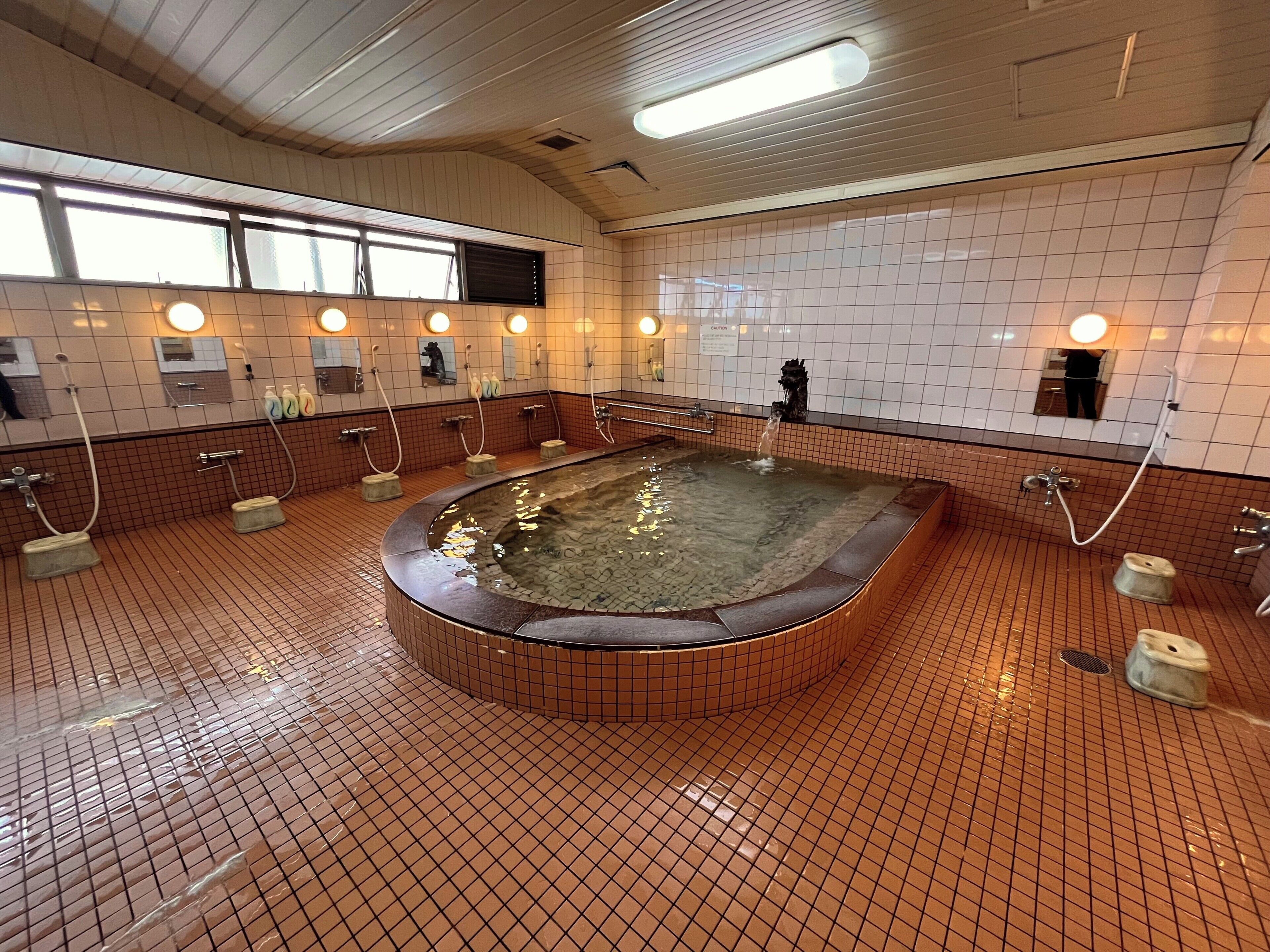 A public bath with multiple showerheads, a central hot tub, and tiled walls.