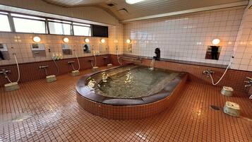 A public bath with multiple showerheads, a central hot tub, and tiled walls.