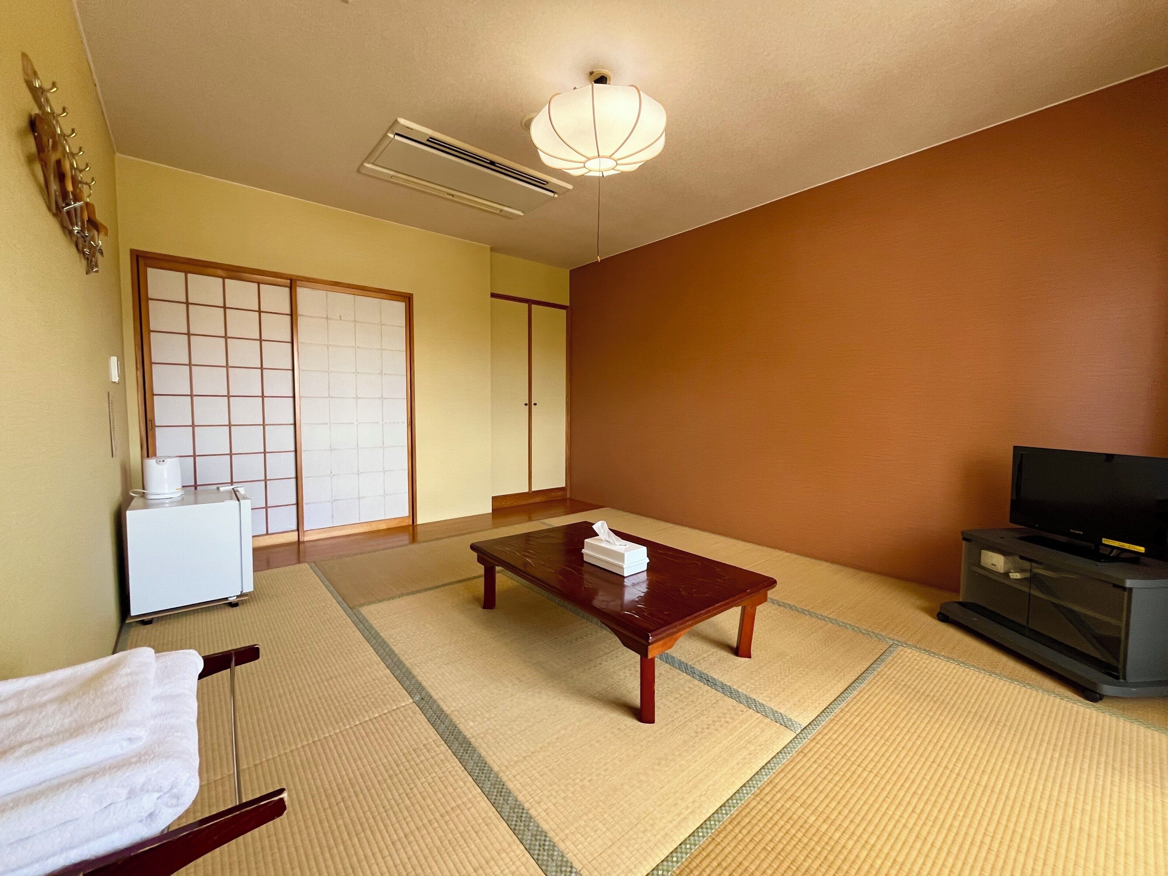 Una habitación japonesa tradicional con suelo de tatami, una mesa baja, un televisor y una puerta corredera.