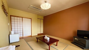 A traditional Japanese room with tatami flooring, a low table, a television, and a sliding door. - Enagic OKinawaInternational Youth Hostel (Naha)