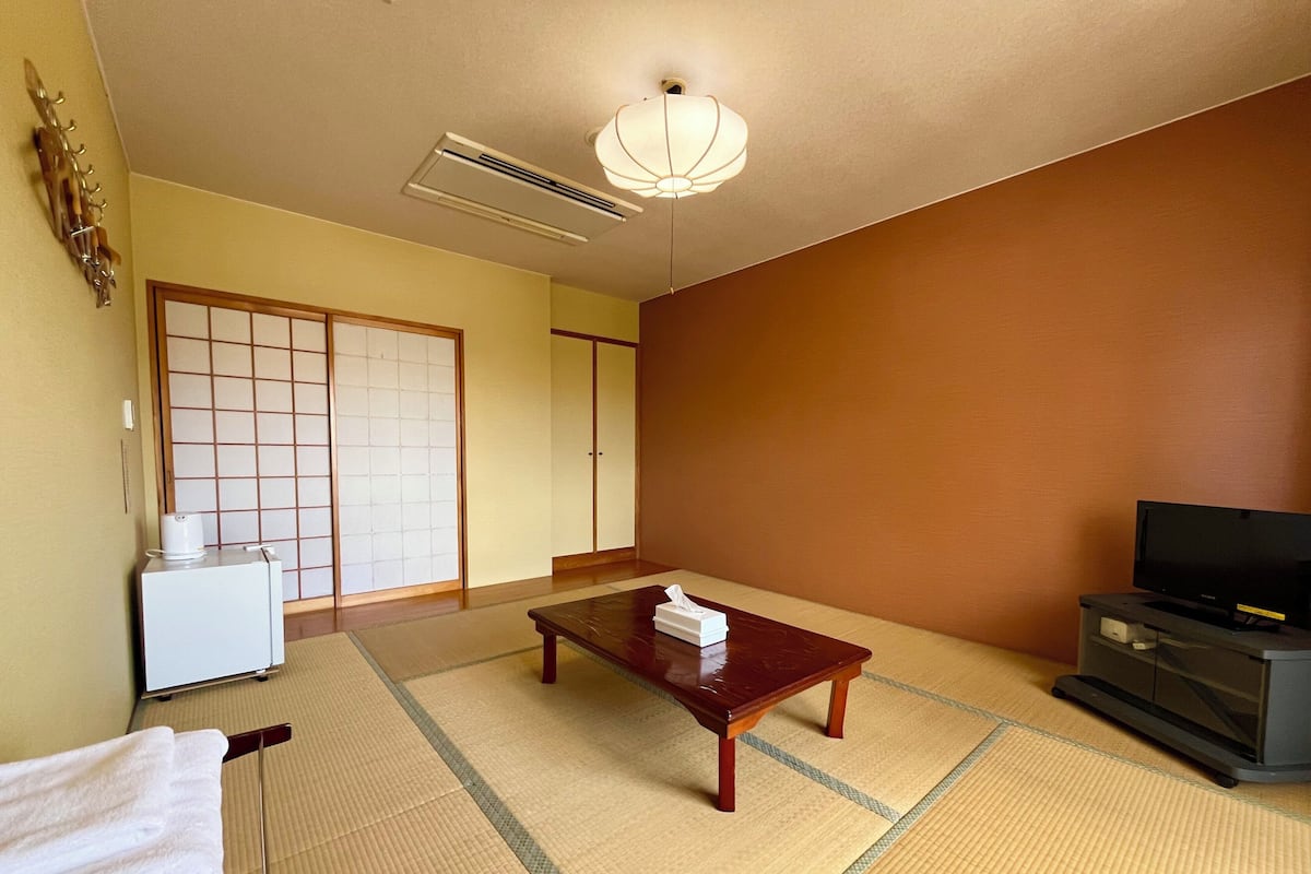 A traditional Japanese room with tatami flooring, a low table, a television, and a sliding door.