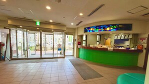 A hotel lobby with a green reception desk, a glass door entrance, and a tiled floor. - Enagic OKinawaInternational Youth Hostel (Naha)