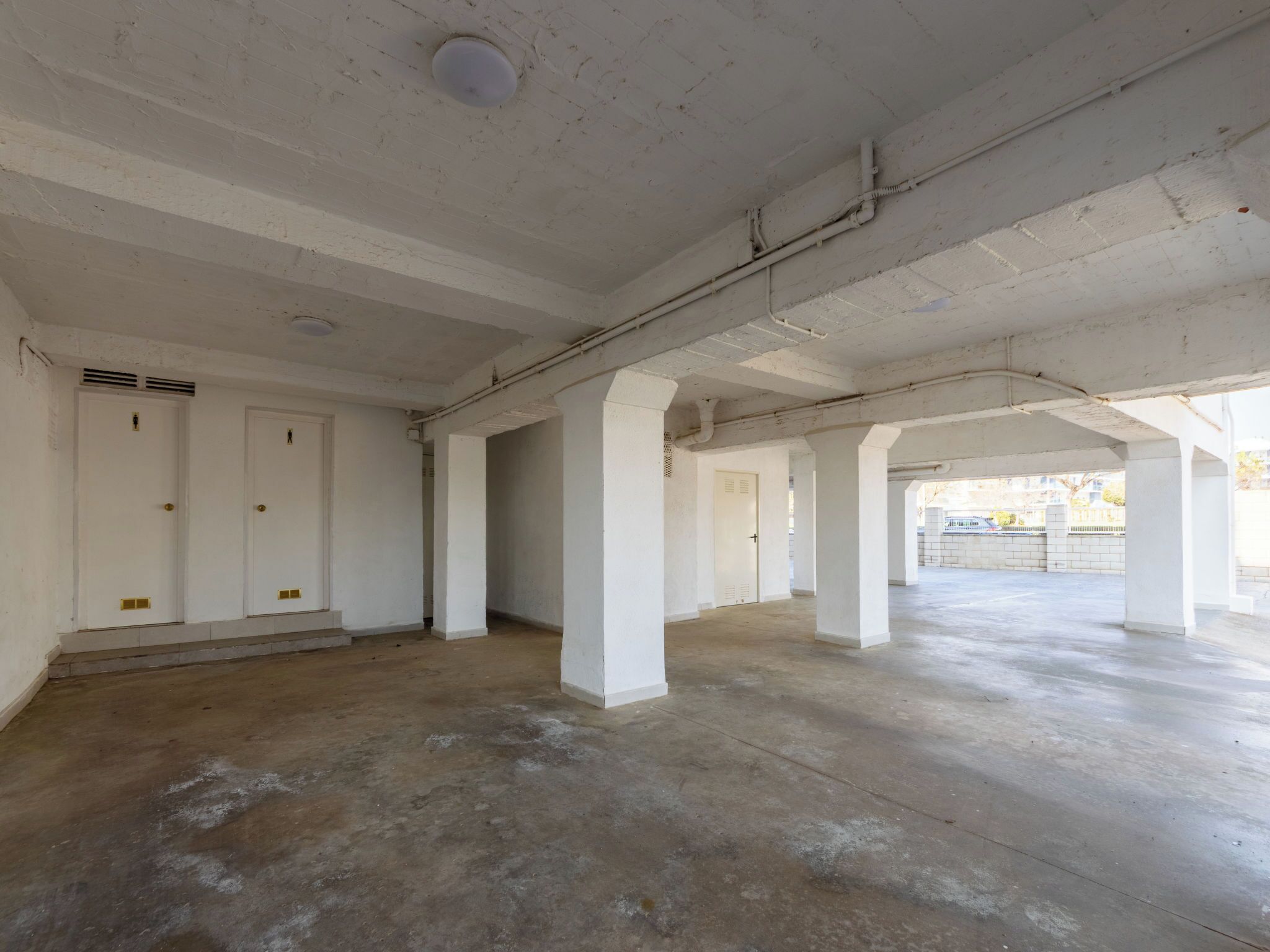 An empty interior with white walls, a concrete floor, and multiple doorways leading to other rooms.