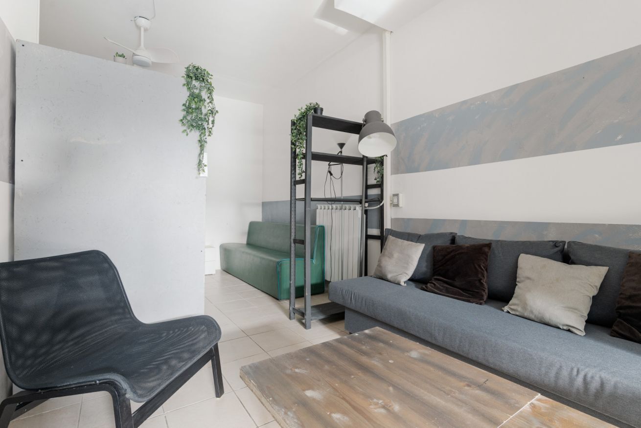 Een moderne woonkamer met een grijze bank, een zwarte stoel, een houten salontafel, een radiator en een hangplant.