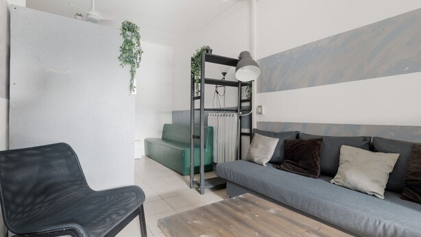 Ein modernes Wohnzimmer mit grauem Sofa, einem schwarzen Sessel, einem Holztisch, einer Heizung und einer hängenden Pflanze.