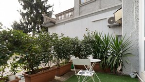 Ein kleiner Patio-Bereich mit einem weißen Klappstuhl, einem Tisch und mehreren Kübelpflanzen.