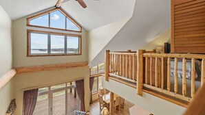 Una habitación con techos altos, ventilador de techo, ventanas amplias, una terraza de madera y una escalera.