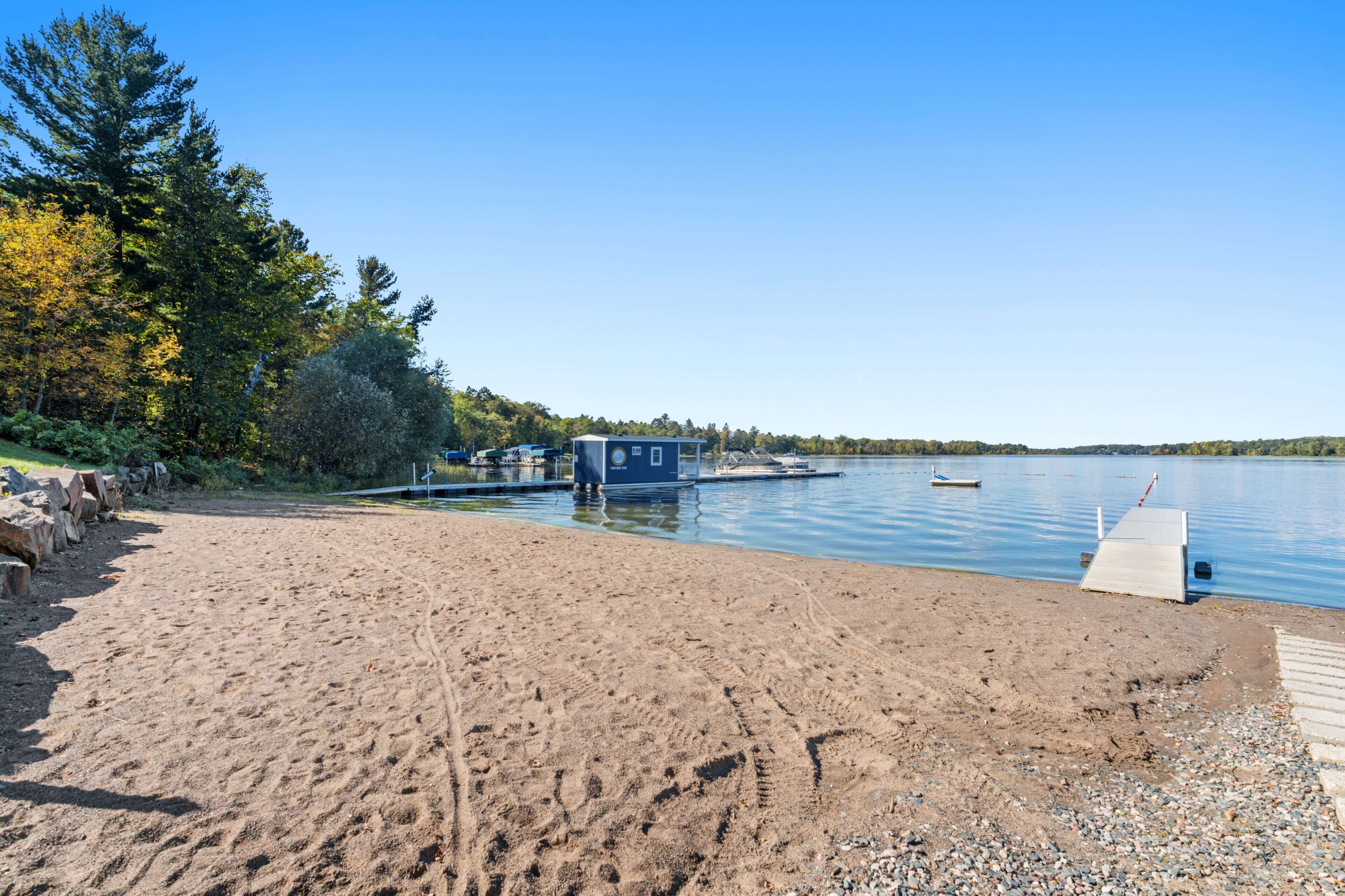 A sandy beach with a dock and boats, surrounded by trees and a clear sky.