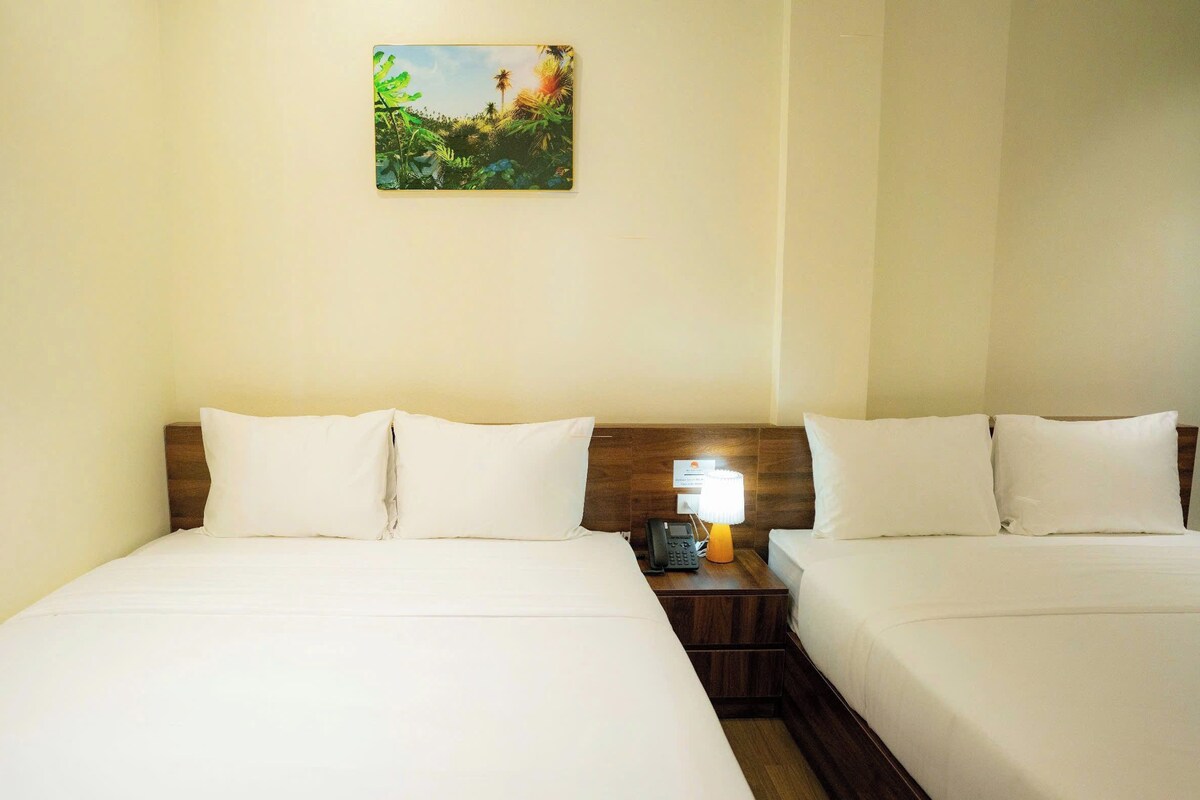 Quarto de hotel com duas camas, mesa de cabeceira com abajur e um quadro na parede.