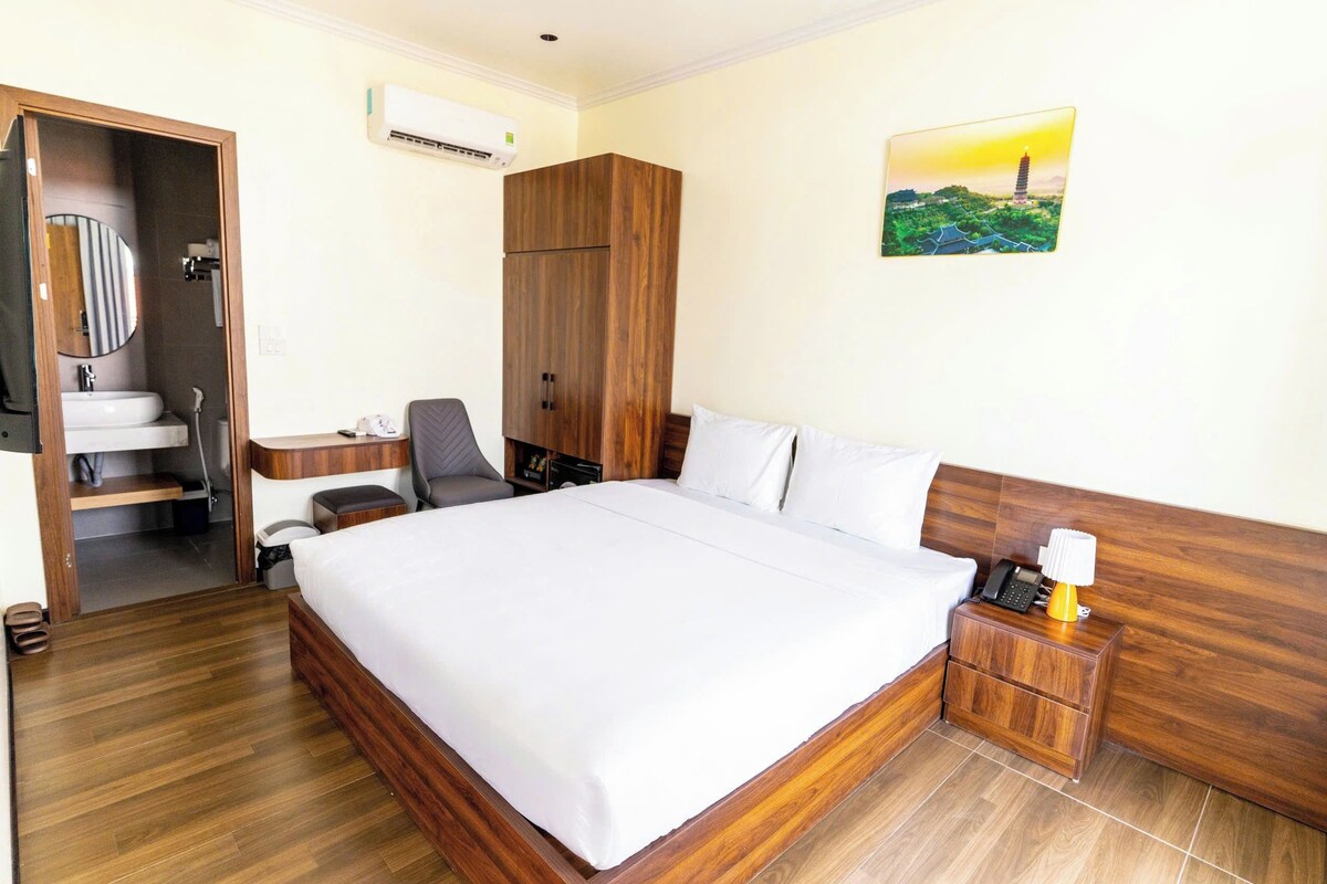Quarto de hotel com cama, escrivaninha, cadeira, guarda-roupa, banheiro e um quadro na parede.