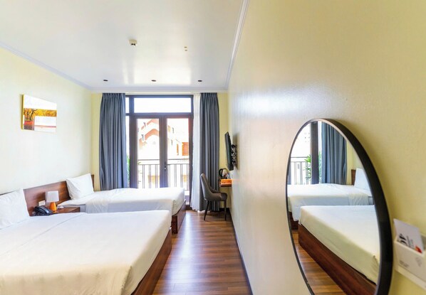 Quarto de hotel com duas camas, uma mesa de trabalho, uma cadeira, um espelho e uma janela com cortinas.
