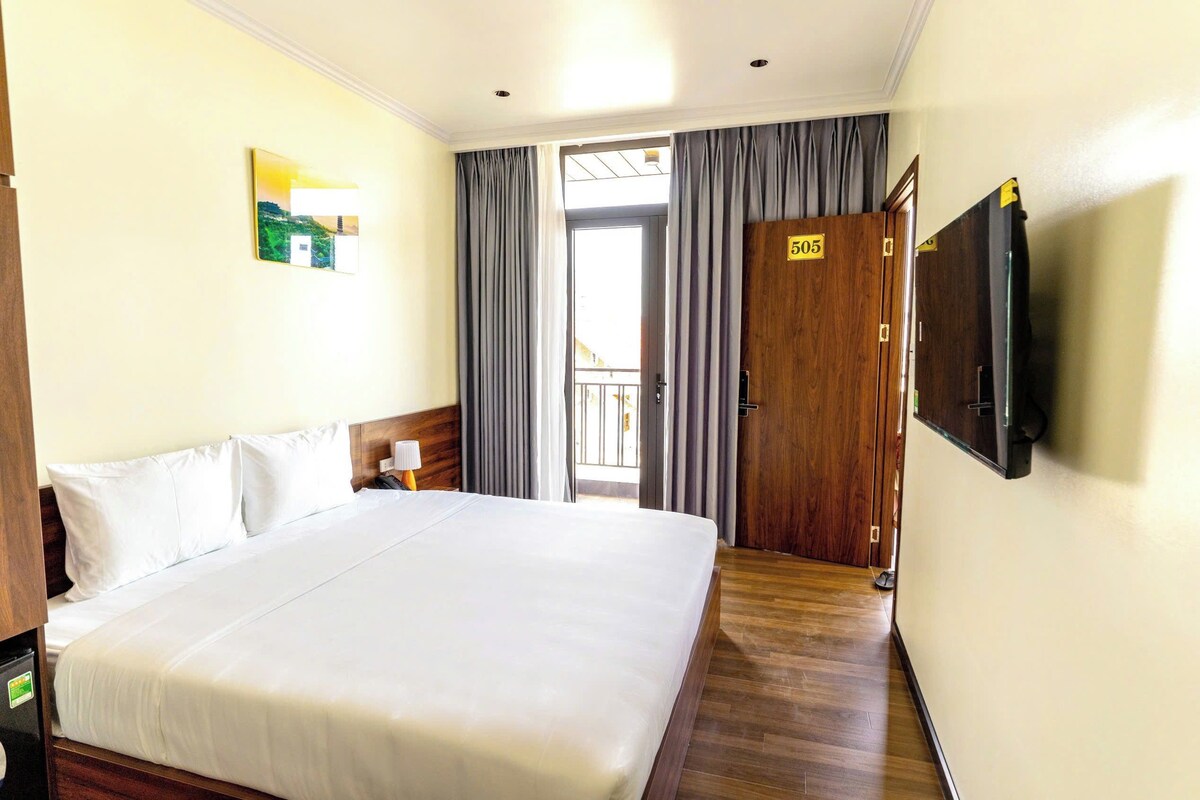 Quarto de hotel com uma cama grande, televisão fixada na parede e porta com o número 505.
