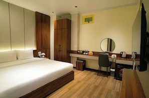 Quarto de hotel com cama, escrivaninha, cadeira, lixeira pequena e espelho.