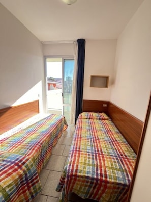 Quarto de hotel com duas camas de solteiro, uma janela pequena e vista para o exterior.