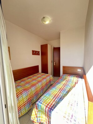 Quarto com duas camas, um guarda-roupa e uma luminária no teto.