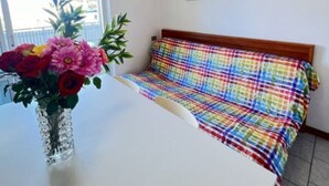 Een kamer met een bed, een witte tafel, een vaas met bloemen en een airconditioning.