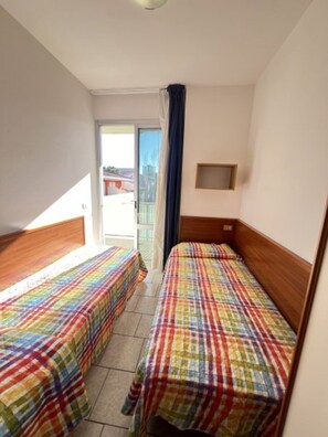 A hotel room with two single beds, a small window, and a view of the outside. - Flat near the beach with terraces (Bibione)