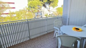 Een balkon met een tafel en stoelen, uitzicht op bomen, en een gebouw op de achtergrond.