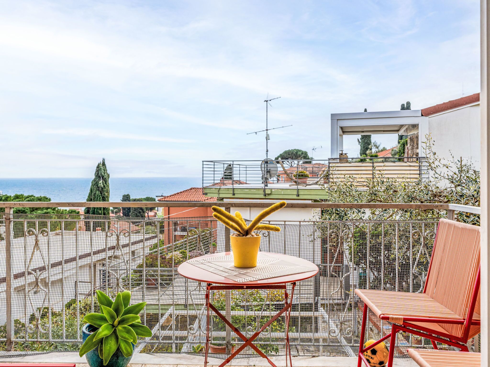 A balcony with a table and chairs, a potted plant, and a view of the sea.