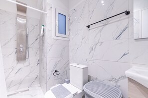 Un baño moderno con ducha, inodoro y lavamanos, todo con paredes de mármol.
