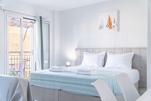 A hotel room with a bed, a nightstand, a window with curtains, and a painting of sailboats. - Studio Apartment 'Corfu Haven' with Balcony, Wi-Fi and Air Conditioning (Kerkira)