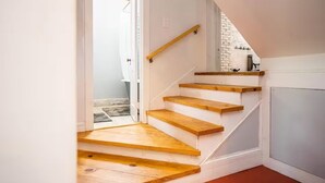 Una escalera de madera con barandilla que lleva a una habitación con pared blanca y una pared de ladrillo decorativa.