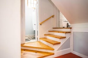 A staircase with wooden steps and a handrail, leading to a room with a white wall and a brick accent wall. - Brick & Beam Studio-Minutes away from Atlanta! (Atlanta)