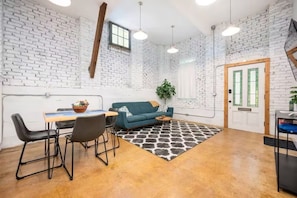 A room with a brick wall, a wooden door, a sofa, a dining table with chairs, and pendant lighting. - Brick & Beam Studio-Minutes away from Atlanta! (Atlanta)
