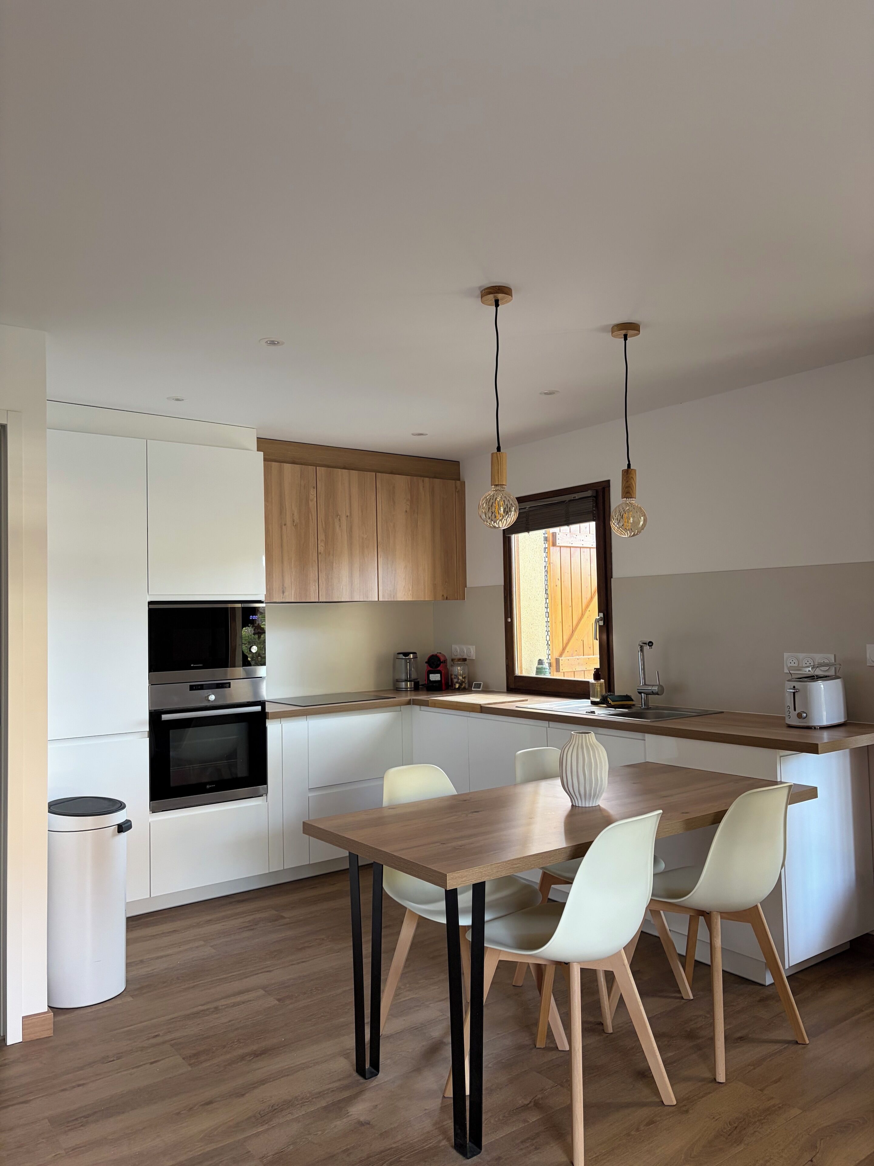 Uma cozinha moderna com eletrodomésticos embutidos, uma área de refeições com mesa e cadeiras de madeira e iluminação pendente.