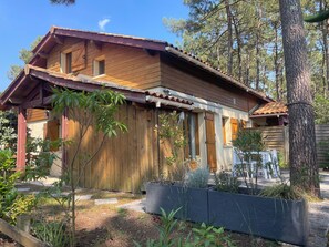 A wooden cabin with a sloped roof, a wooden deck, and a garden area with various plants. - Renovated house in the heart of the pine forest - Swimming pool - 4 people - Lacanau Océan (Lacanau)