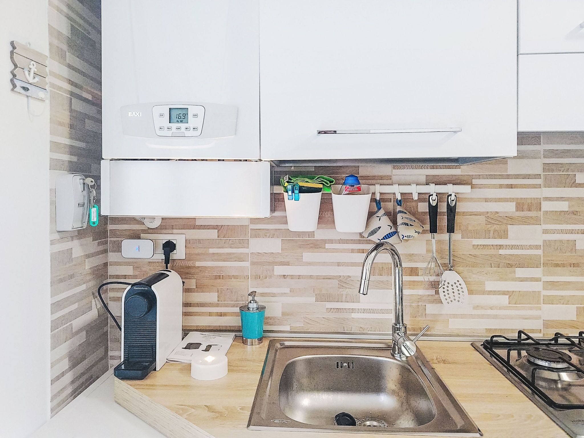 Una cucina con lavello in acciaio inossidabile, piano cottura a gas, forno integrato, macchina da caffè e bilancia da parete.