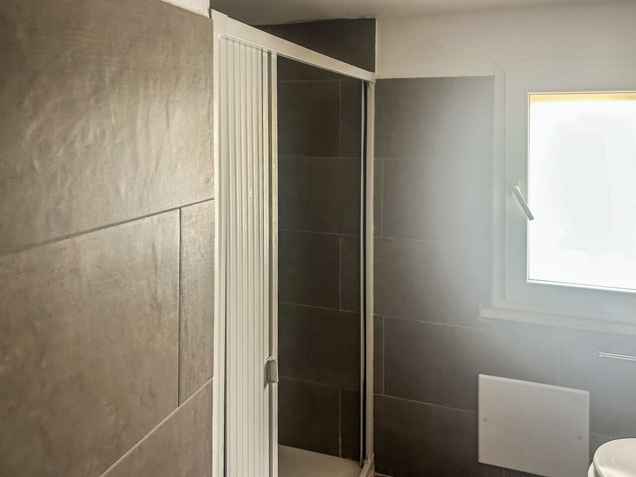 A bathroom with a shower, tiled walls, and a window.