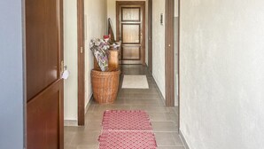 Un pasillo con puertas de madera, una cesta de mimbre con flores y un tapete rojo con estampado.