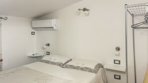 Un dormitorio con cama, aire acondicionado de pared, lámpara colgante, mesita de noche y estante en la pared.