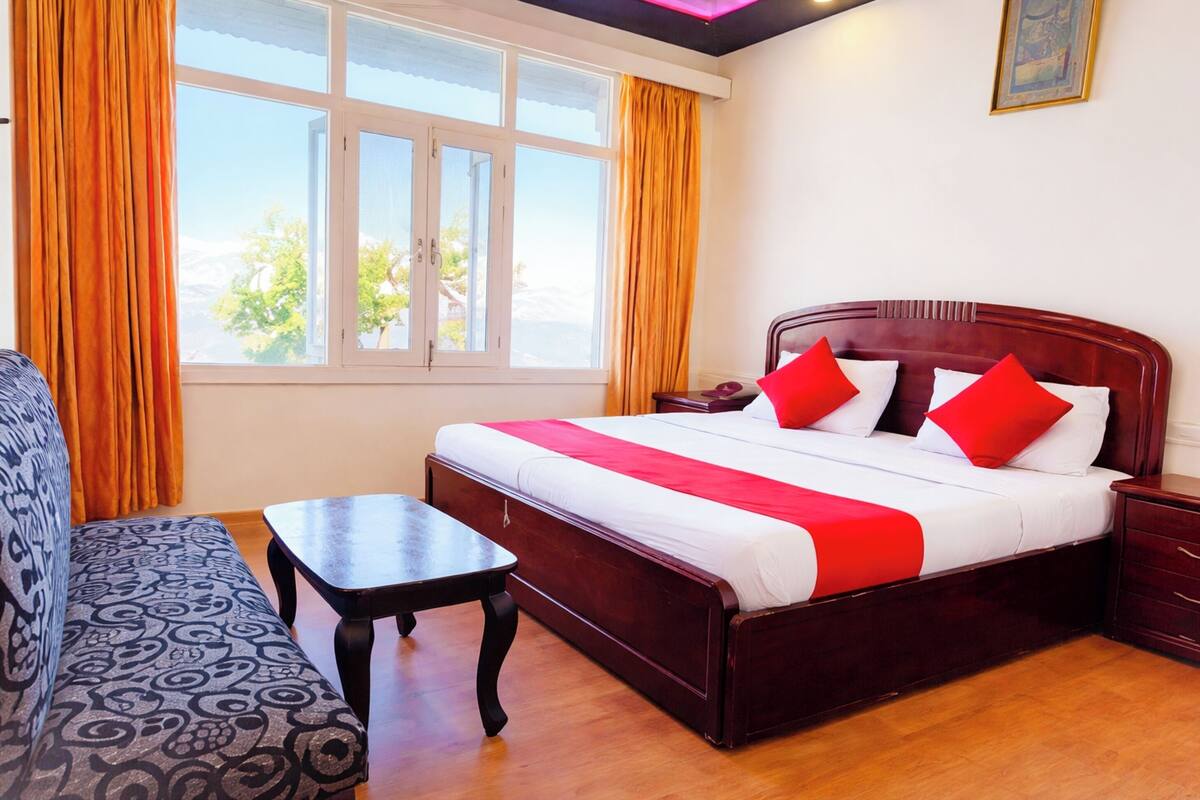 A hotel room with a bed, a sofa, a small table, and a window with curtains.