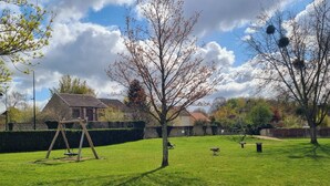 Un área verde con césped, un columpio, un árbol y un muro de piedra.