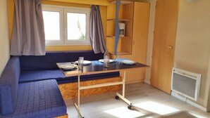 Habitación compacta con kitchenette, ventana con cortinas, sofá y una pequeña mesa con cafetera.