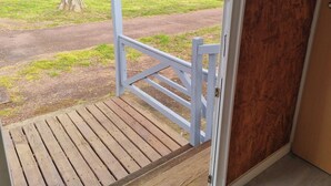 Una terraza de madera con barandilla blanca que da a un área cubierta de césped, con árboles y un sendero.