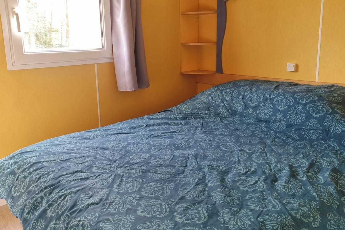 Una habitación con cama, ventana con cortinas y una estantería.