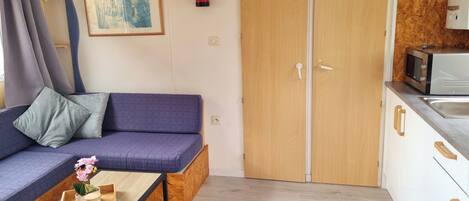 A compact room with a sofa, a small table with a candle and flowers, a microwave, and a wooden cabinet.