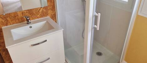 A bathroom with a white sink, a mirror, a shower with a glass door, and a wooden floor.