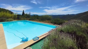 Une piscine rectangulaire avec une terrasse en bois, entourée d’une végétation luxuriante et bordée de collines en arrière-plan.