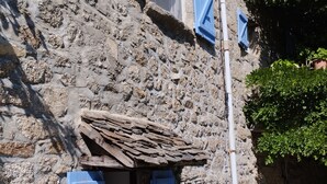 Un bâtiment en pierre avec des volets bleus, une porte en bois et une petite table accompagnée d’une chaise.
